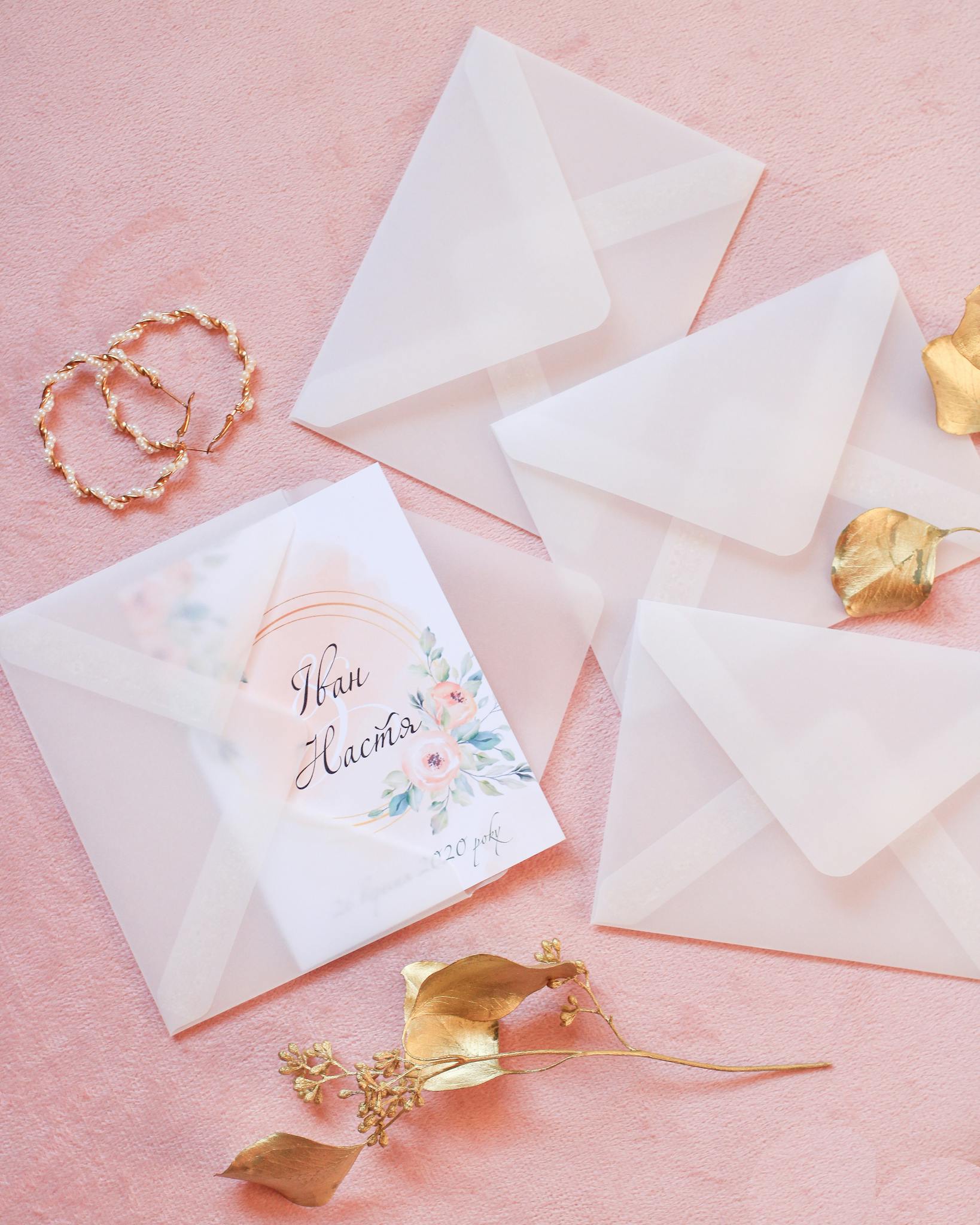 A minimalist wedding invitation with floral elements on a pink background, featuring elegant envelopes.