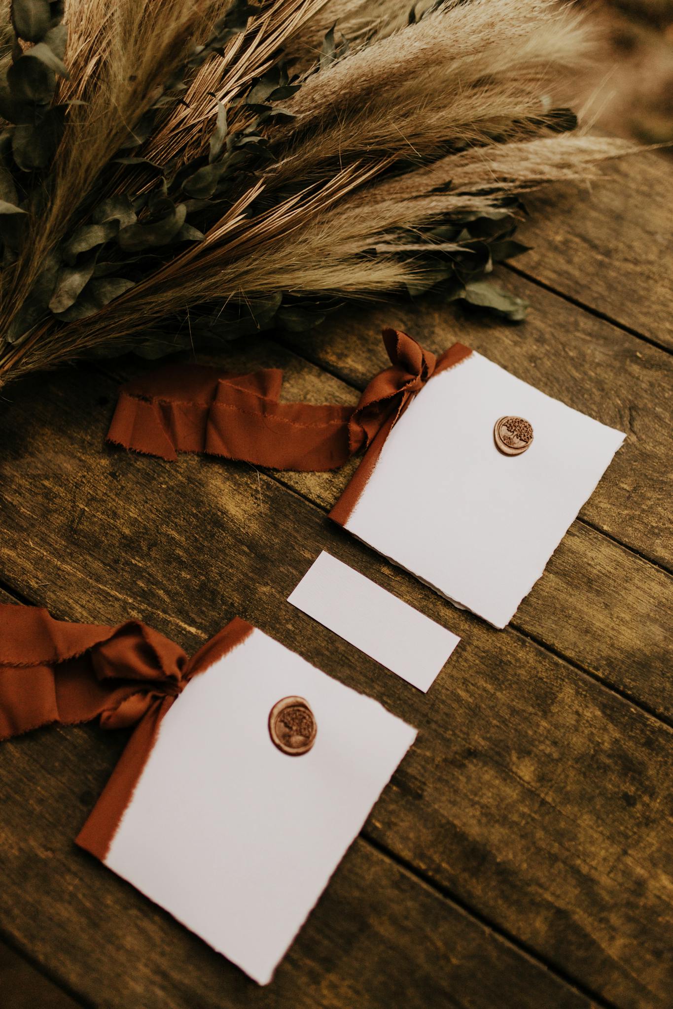 Elegant rustic wedding invitations with wax seal on a wooden table with flowery decor.